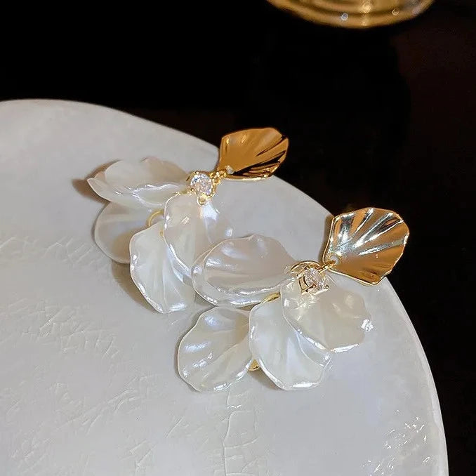 Earrings with gold and white elements on a textured surface, branded 'GLAMOUR GIRL'.