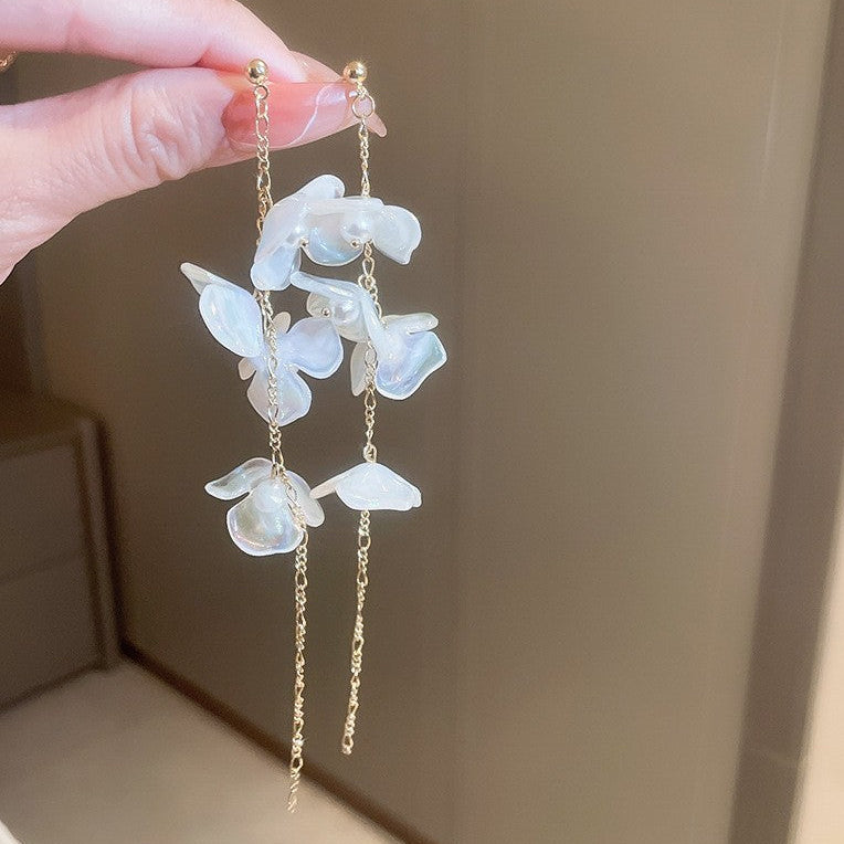 Elegant earrings with floral designs held by a hand against a neutral background