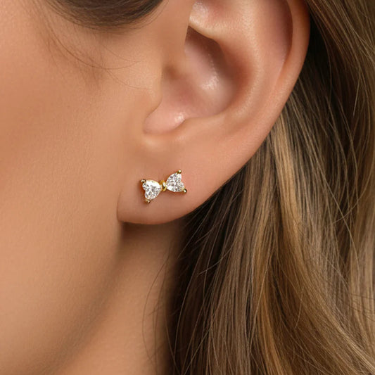 Close-up of an ear wearing a gold bow-shaped earring with a clear gemstone.