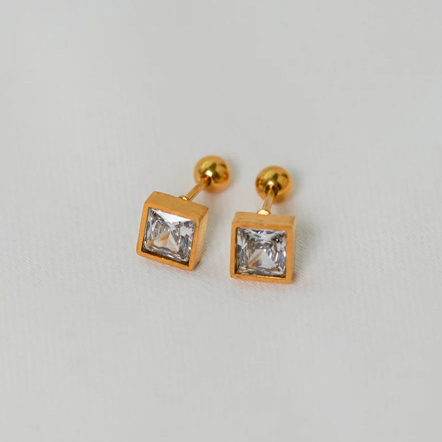 Gold square earrings with clear gemstones on a light gray background