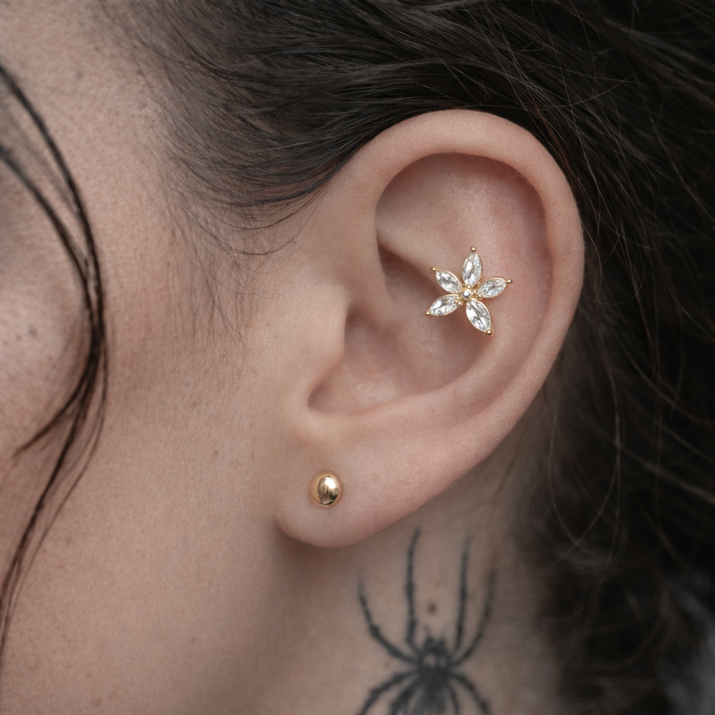 Close-up of an ear with a gold earring and a floral silver earring, featuring a spider tattoo on the neck.