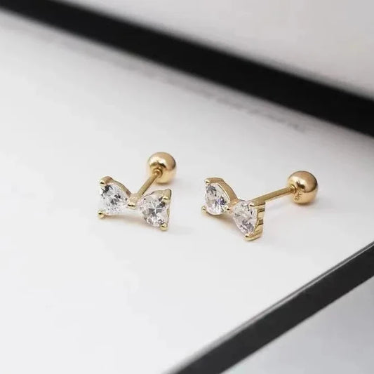 Gold bow-shaped earrings with clear gemstones on a light gray surface.