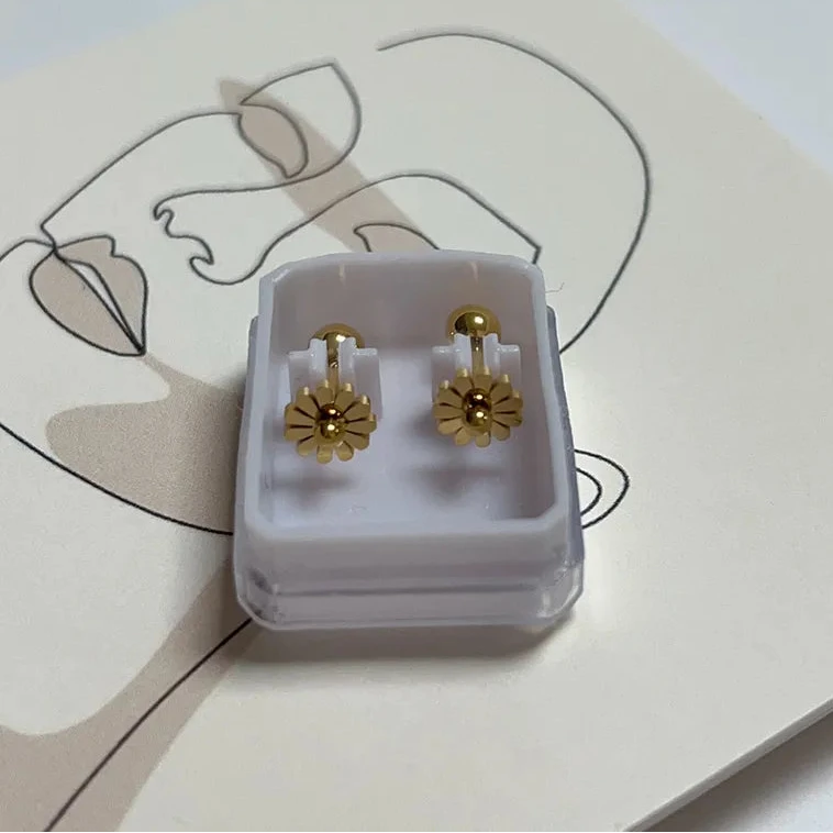 Gold flower-shaped earrings in a clear jewelry box on a white background