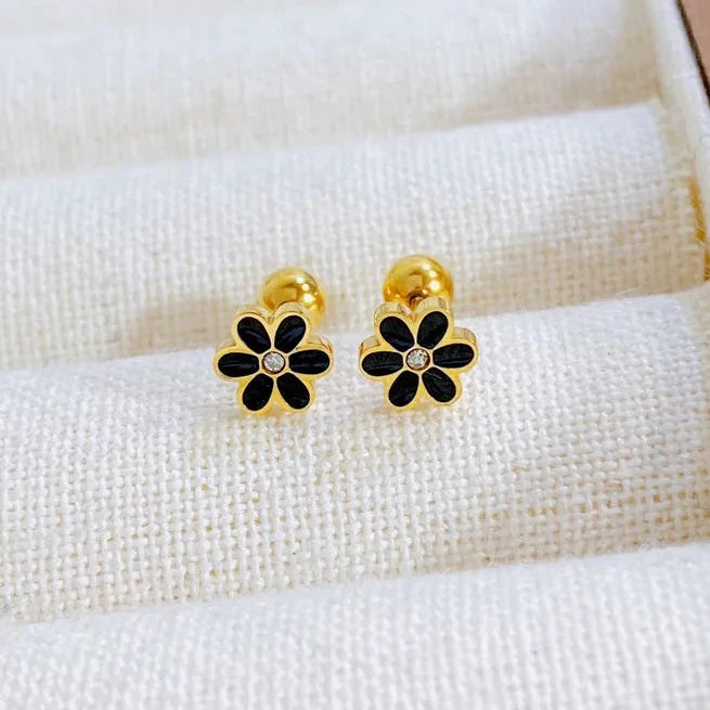 Gold and black flower-shaped earrings on a white fabric background