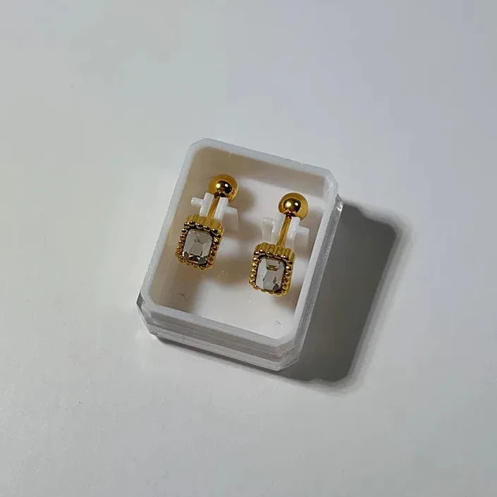 Gold earrings with clear stones in a clear box on a white background