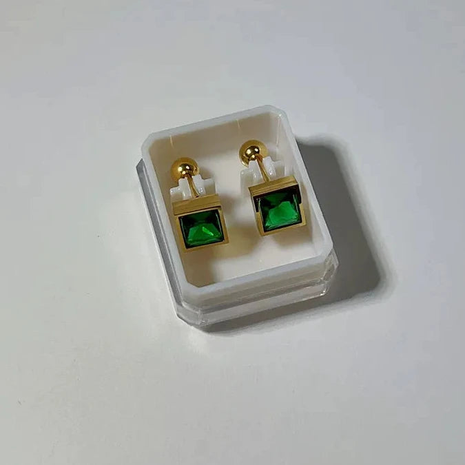 Gold earrings with green gemstones in a clear display case on a white background