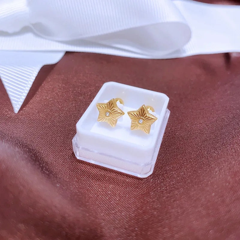 Gold star earrings in a clear box on a brown fabric background