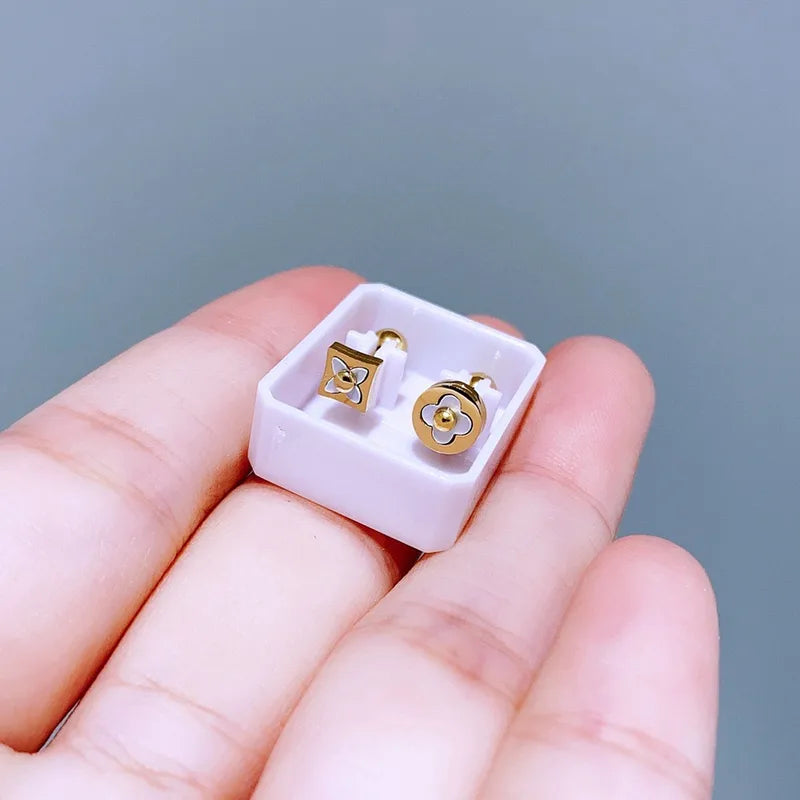 Gold earrings in a white box held by a hand against a gray background