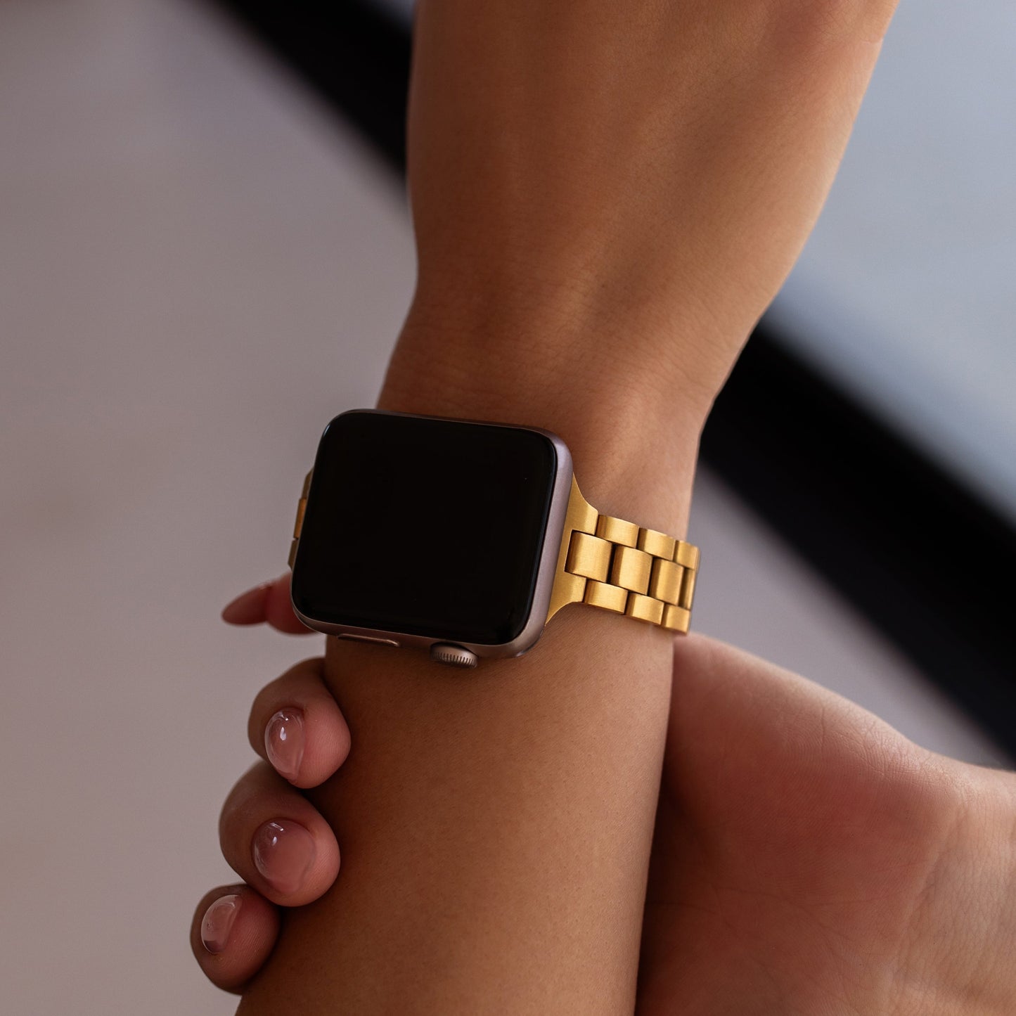 Smartwatch with a gold band on a wrist against a neutral background