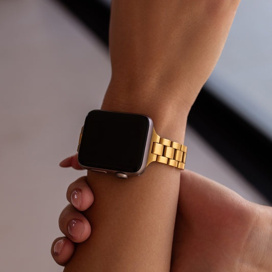 Smartwatch with a gold band on a wrist against a neutral background