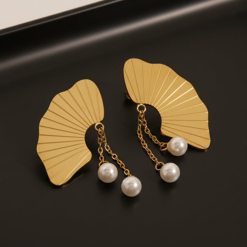 Gold earrings with fan-shaped design and pearl drops on a light background