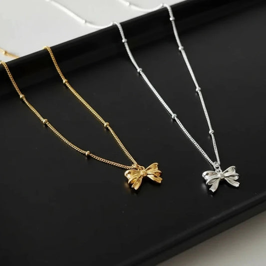 Gold and silver bow-shaped necklaces on a light background
