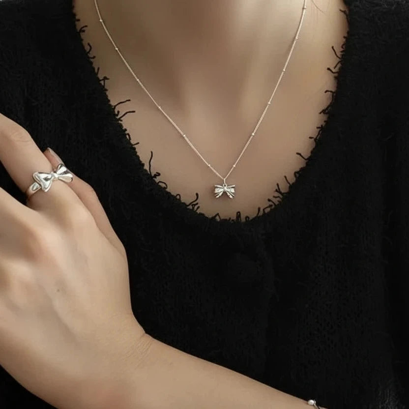 Silver necklace with bow pendant worn by a person against a black background