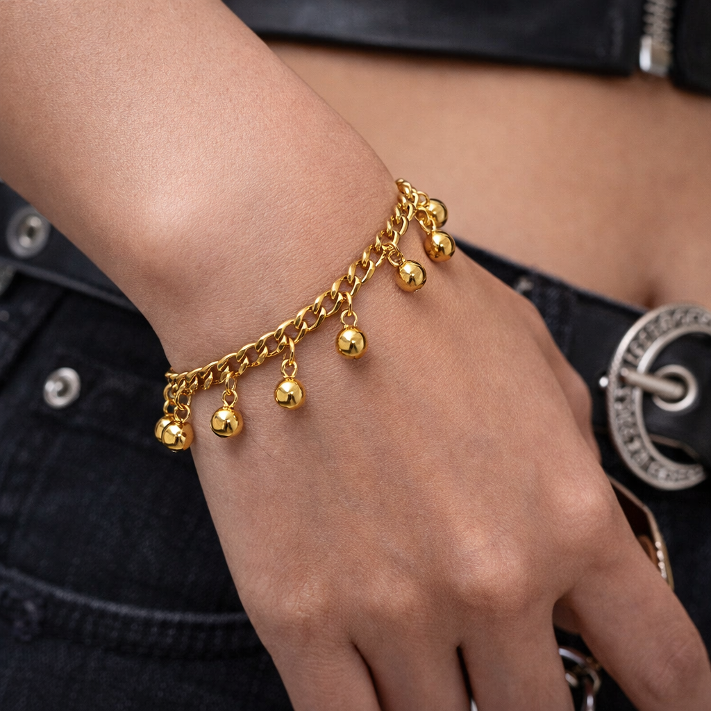 Gold bracelet with hanging beads on a wrist against a black background