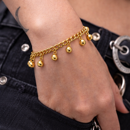 Gold bracelet with hanging charms on a wrist against a dark denim background