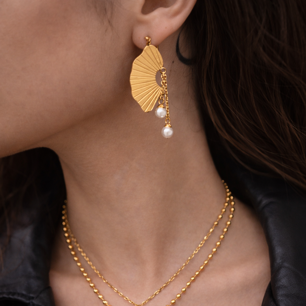 Gold earrings with pearl drops worn by a person against a dark background