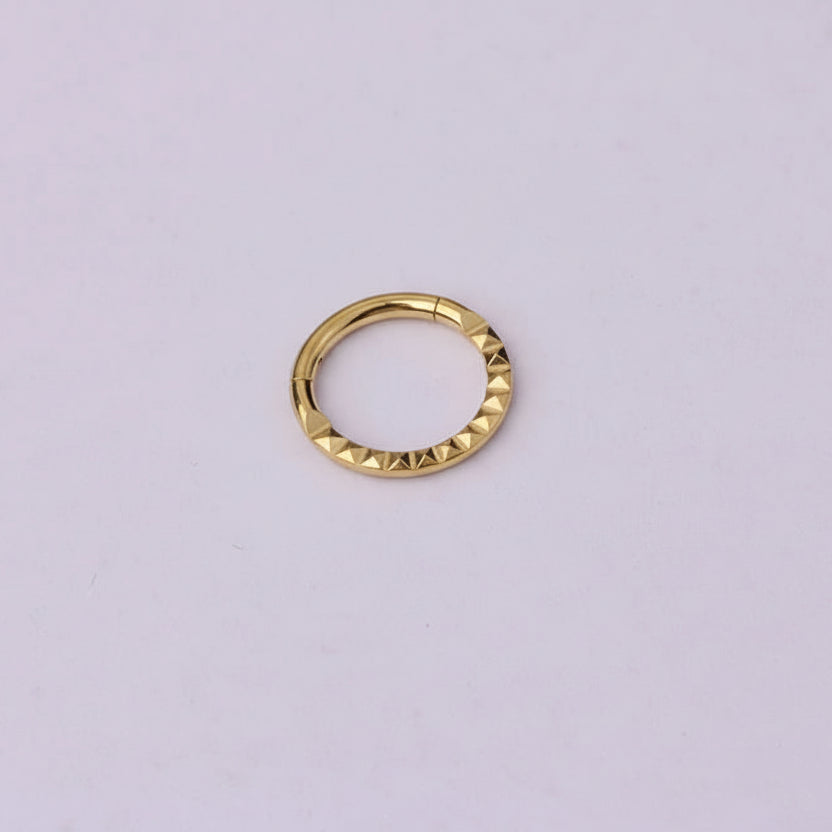 Gold ring with textured design on a light purple background