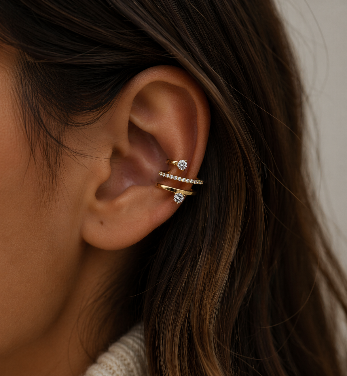 Close-up of an ear wearing gold and diamond earrings with a blurred background